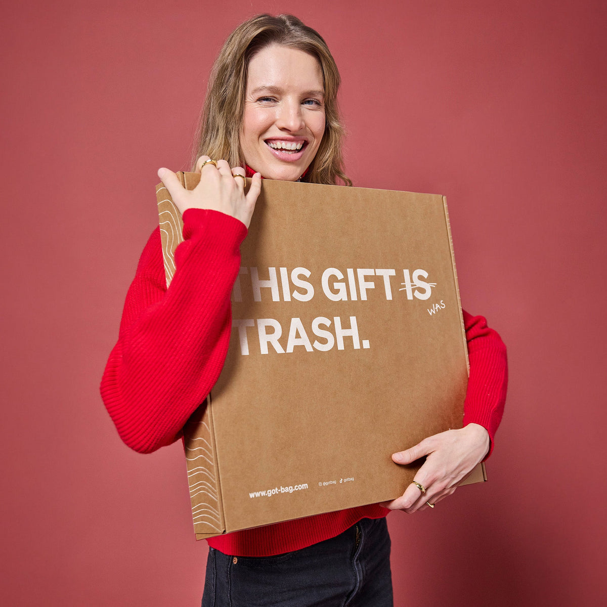 GIFT PACKAGING Accessoires von einer lächelnden Frau mit der Aufschrift THIS GIFT WAS TRASH in den Händen gehalten.