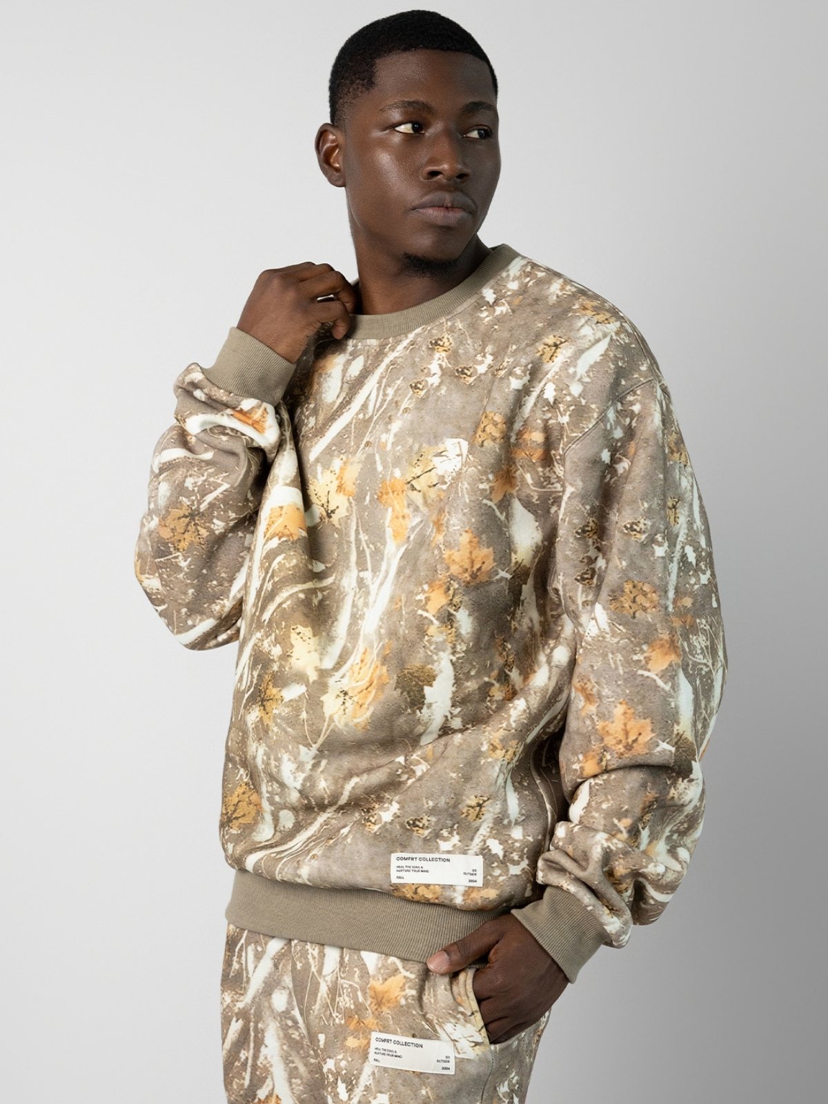 A woman wearing an oversized fit camo crew sweatshirt in a light color with camouflage patterns.